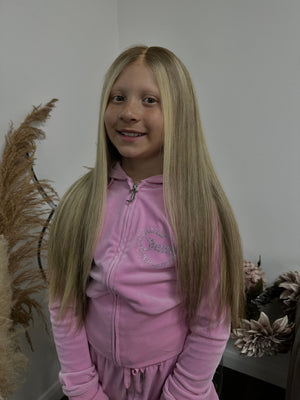 Child wearing a long blonde straight human hair wig, styled naturally,
against a white background – Nuola Wigs.