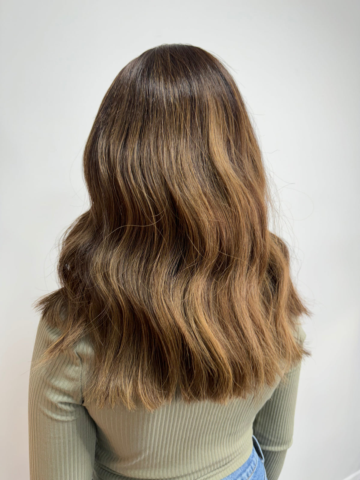 Child wearing a long brown wavy human hair wig, styled naturally,
against a white background – Nuola Wigs.