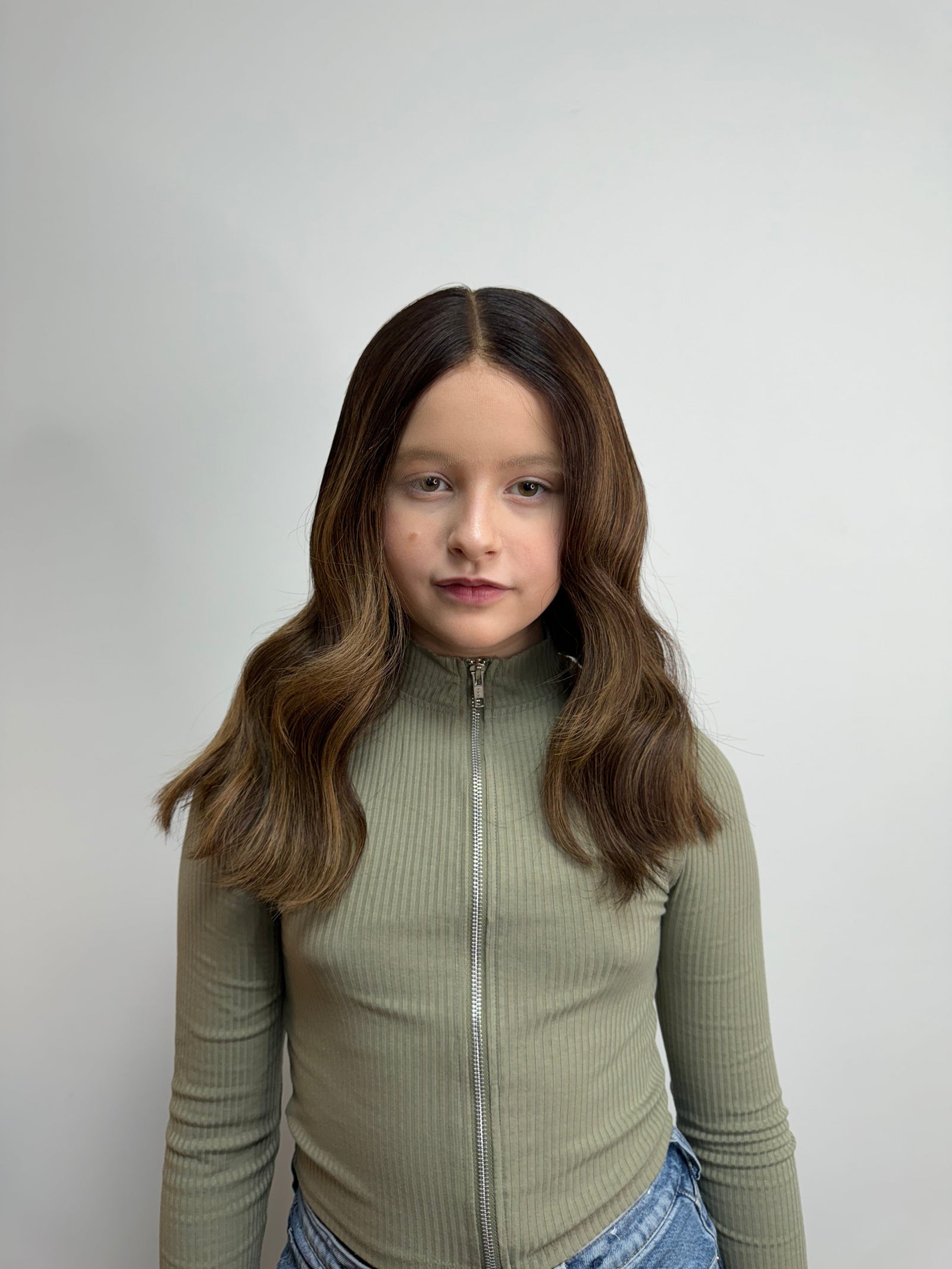 Child wearing a long brown wavy human hair wig, styled naturally,
against a white background – Nuola Wigs