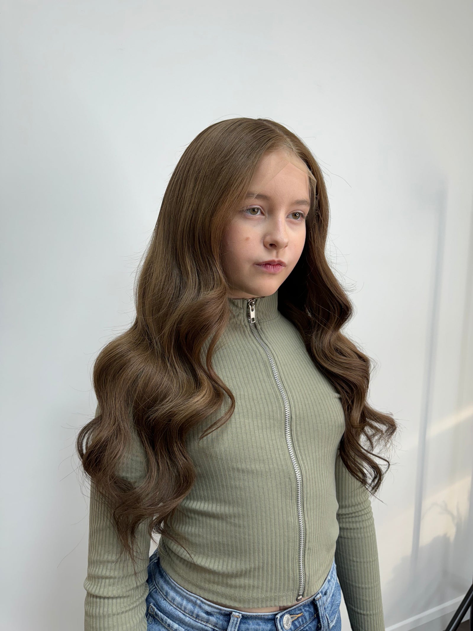 Child wearing a long brown wavy human hair wig, styled naturally,
against a white background – Nuola Wigs.