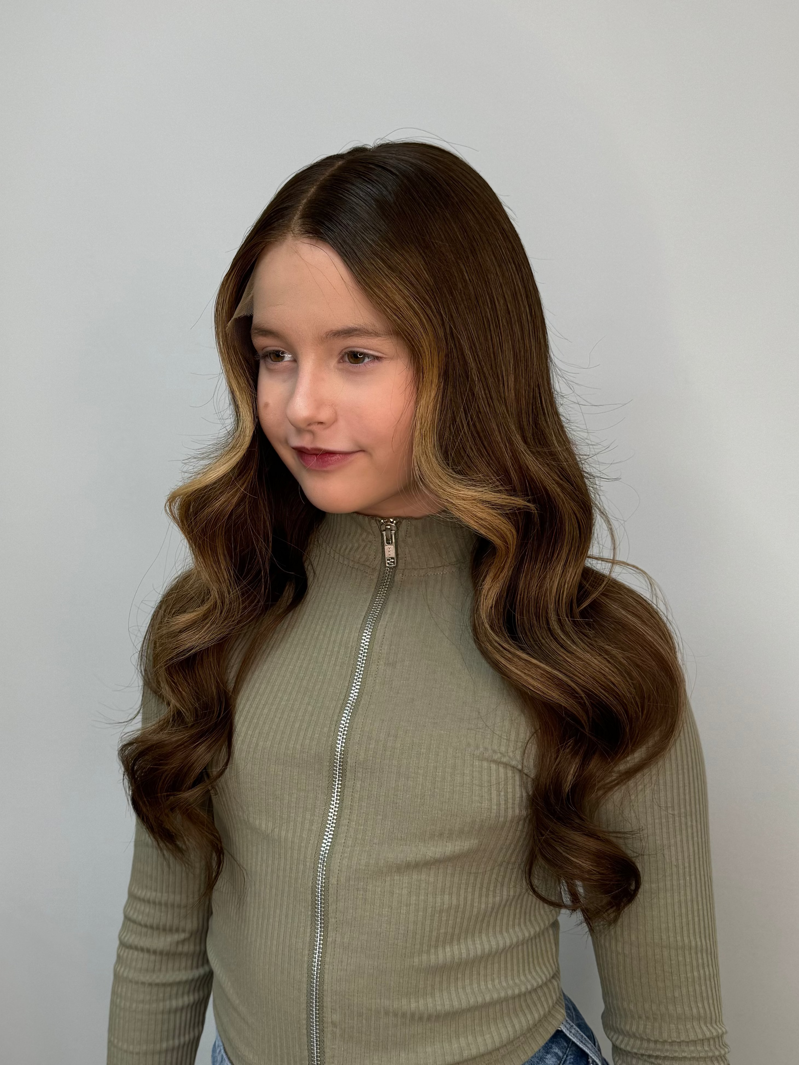 Child wearing a long brown wavy human hair wig, styled naturally,
against a white background – Nuola Wigs.